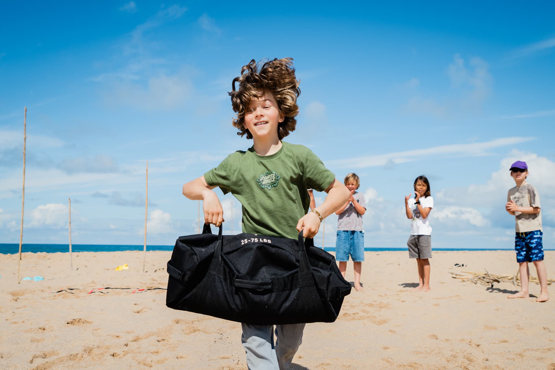 Un garçon porte un sac de sable lourd pendant un défi de fitness sur la plage